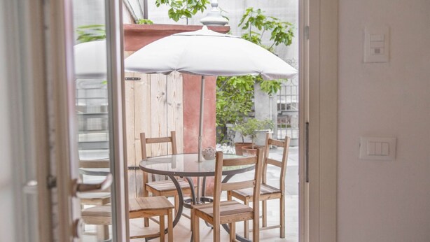 An outdoor patio with a round table and wooden chairs, an umbrella, and a wooden pergola.