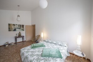 Un dormitori amb un llit, una cadira, una taula i una làmpada.