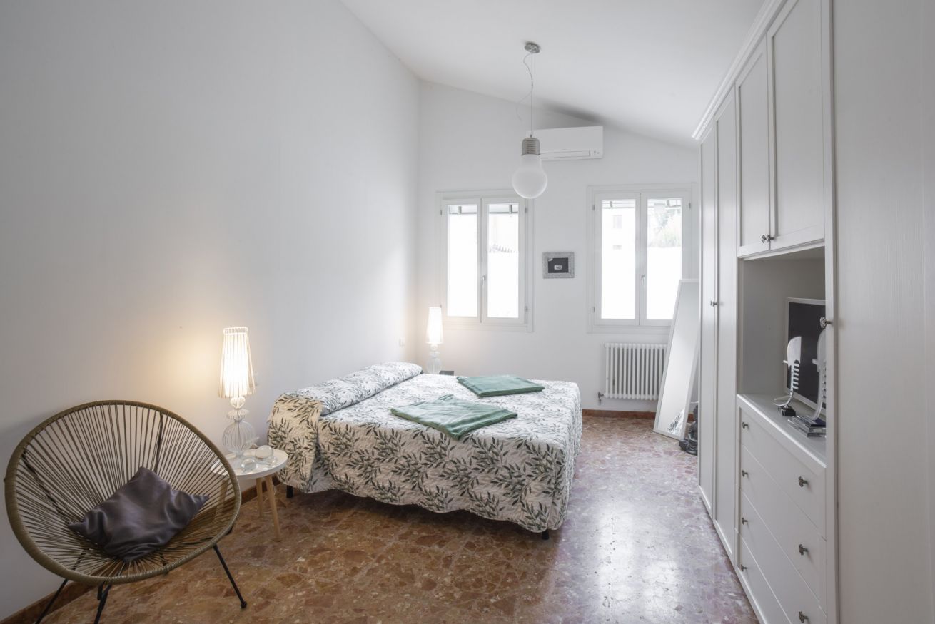 Un dormitorio con cama, sillón, cómoda y radiador.