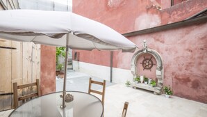 A glass table with chairs and a white umbrella in an outdoor patio area with a pink wall and a decorative archway.