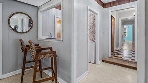 Un pasillo con un banco de madera, un espejo y una puerta que da a otra habitación.