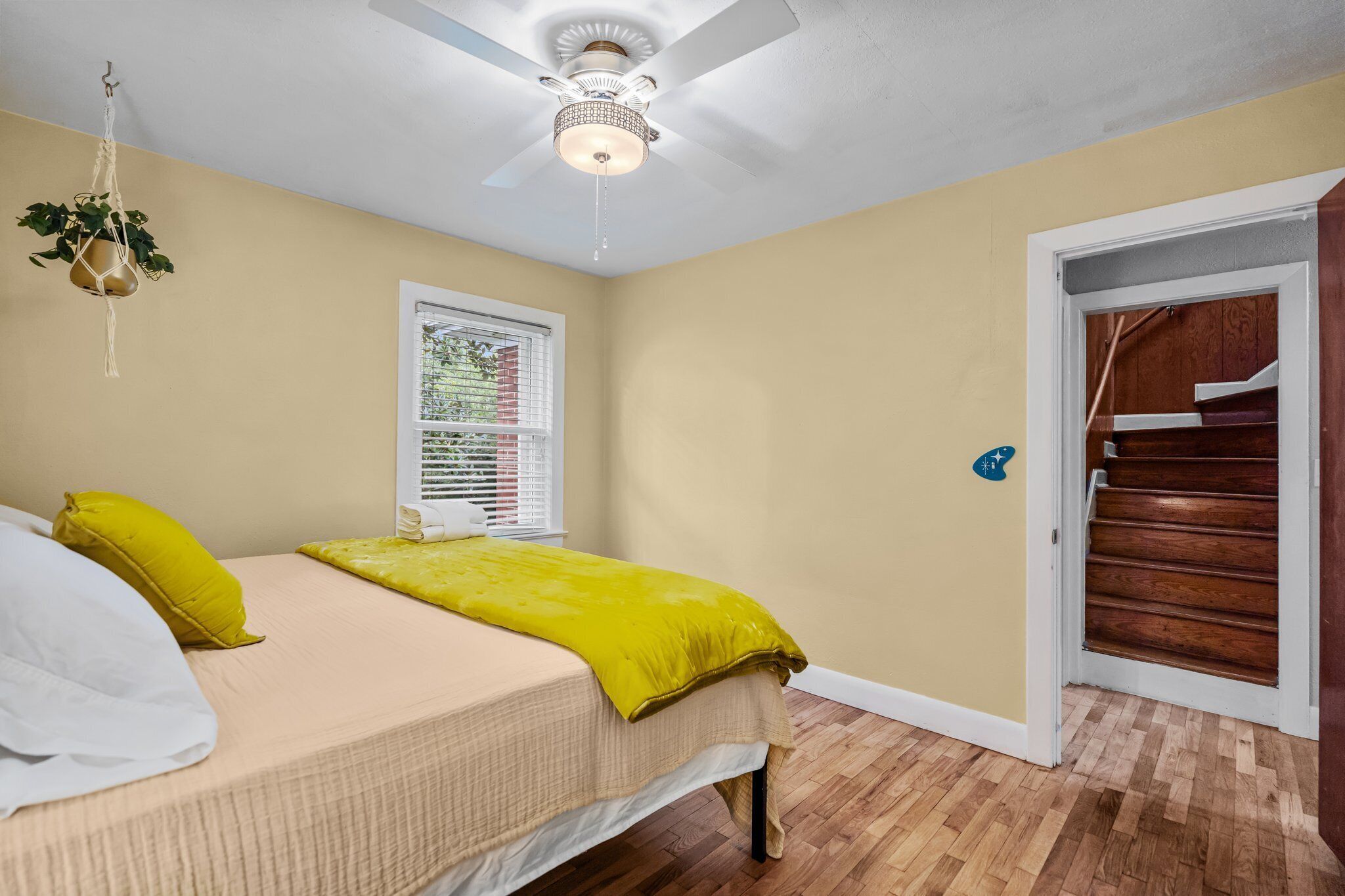 Ein Schlafzimmer mit einem Bett, einem Deckenventilator, einem Fenster mit Jalousien, einer Holztreppe und einer Tür mit Sterndekoration.