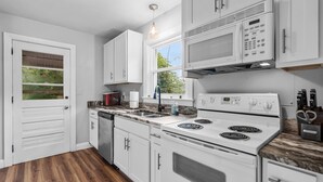 Una cocina con gabinetes blancos, microondas integrado, estufa y lavavajillas.