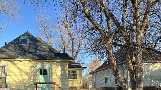 En ejendom kaldet 'The Yellow Bungalow' med et træhegn, et træ og en stol udenfor.