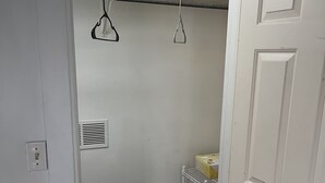 Et garderobeskab med en metalstang, en hylde med en æske, og en dør.