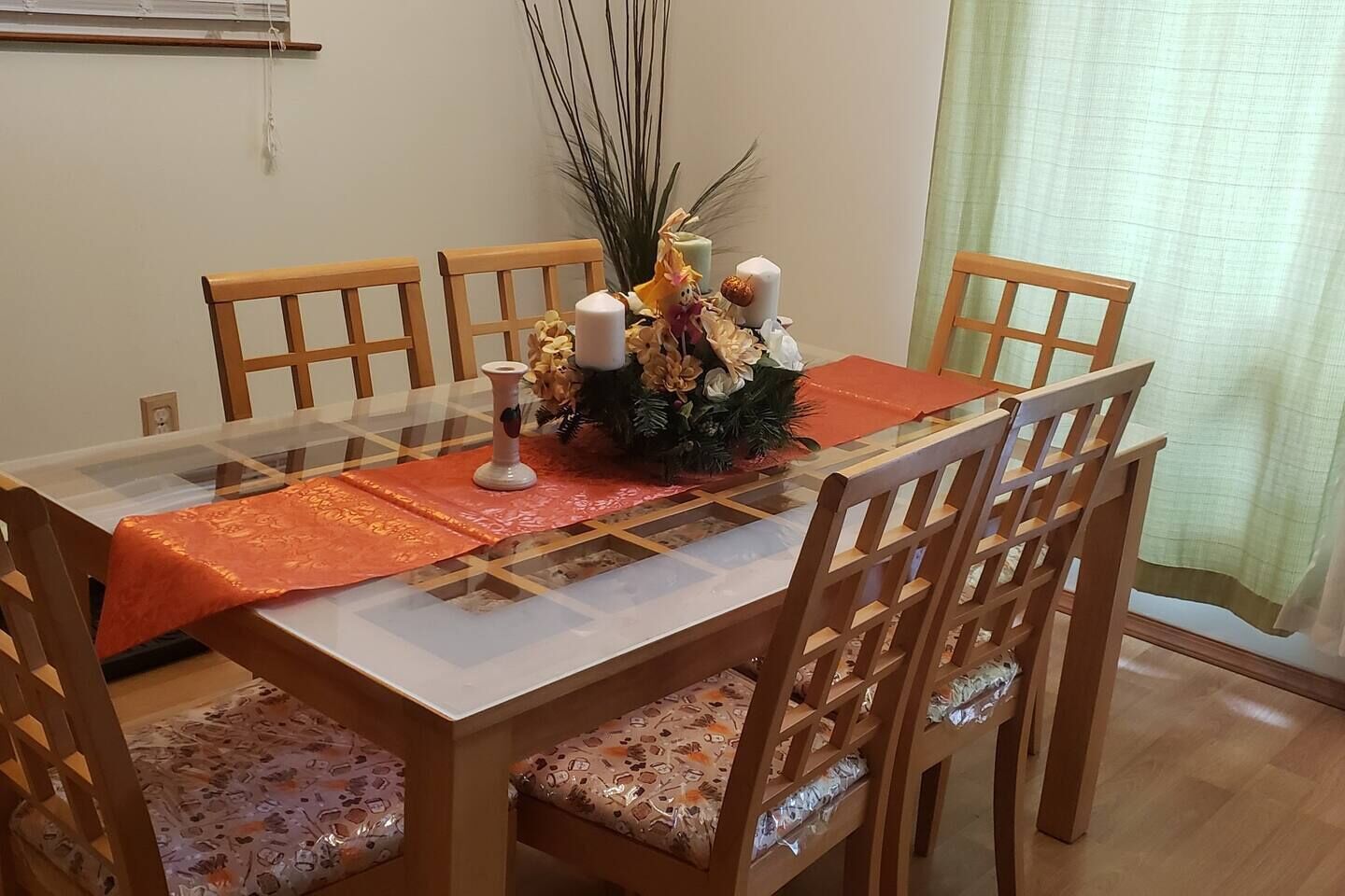 A dining table with six wooden chairs, a glass top, and a centerpiece with candles and dried plants.