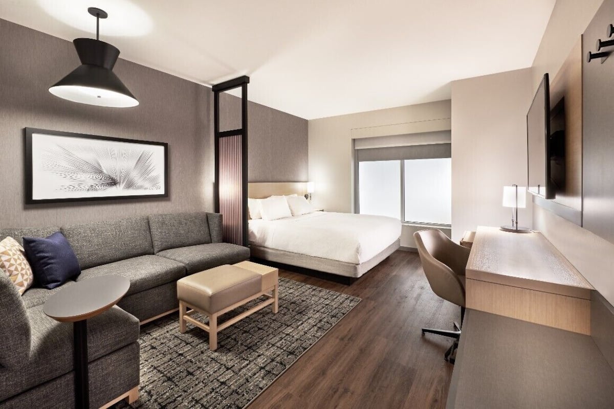 Ett modernt hotellrum med en säng, en soffa, ett skrivbord och ett stort fönster.
