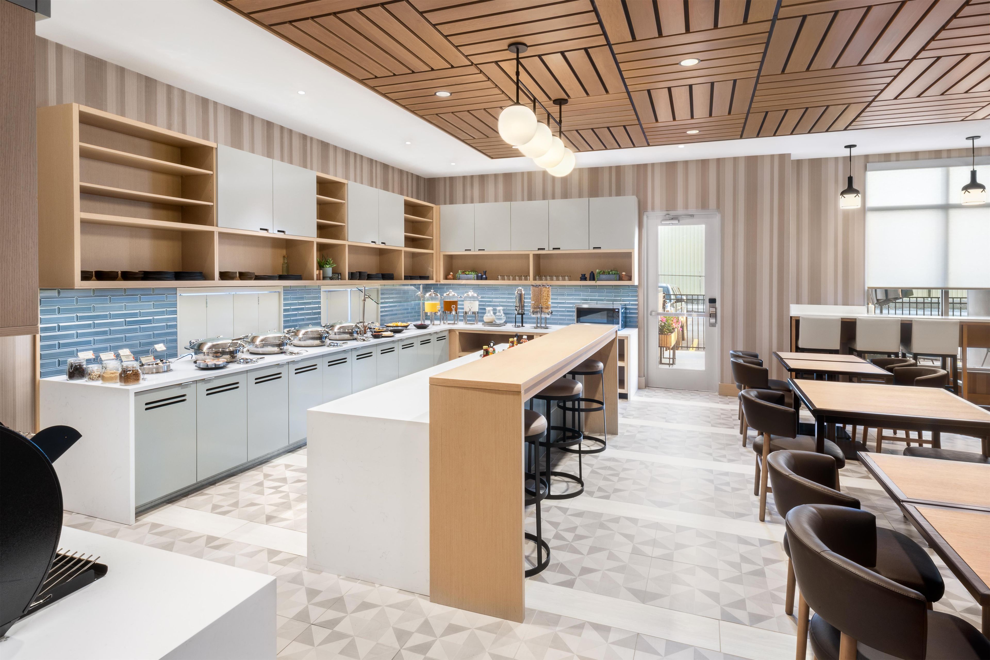 A modern kitchen with a central island, bar stools, and a dining area with tables and chairs.