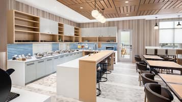 A modern kitchen with a central island, bar stools, and a dining area with tables and chairs.