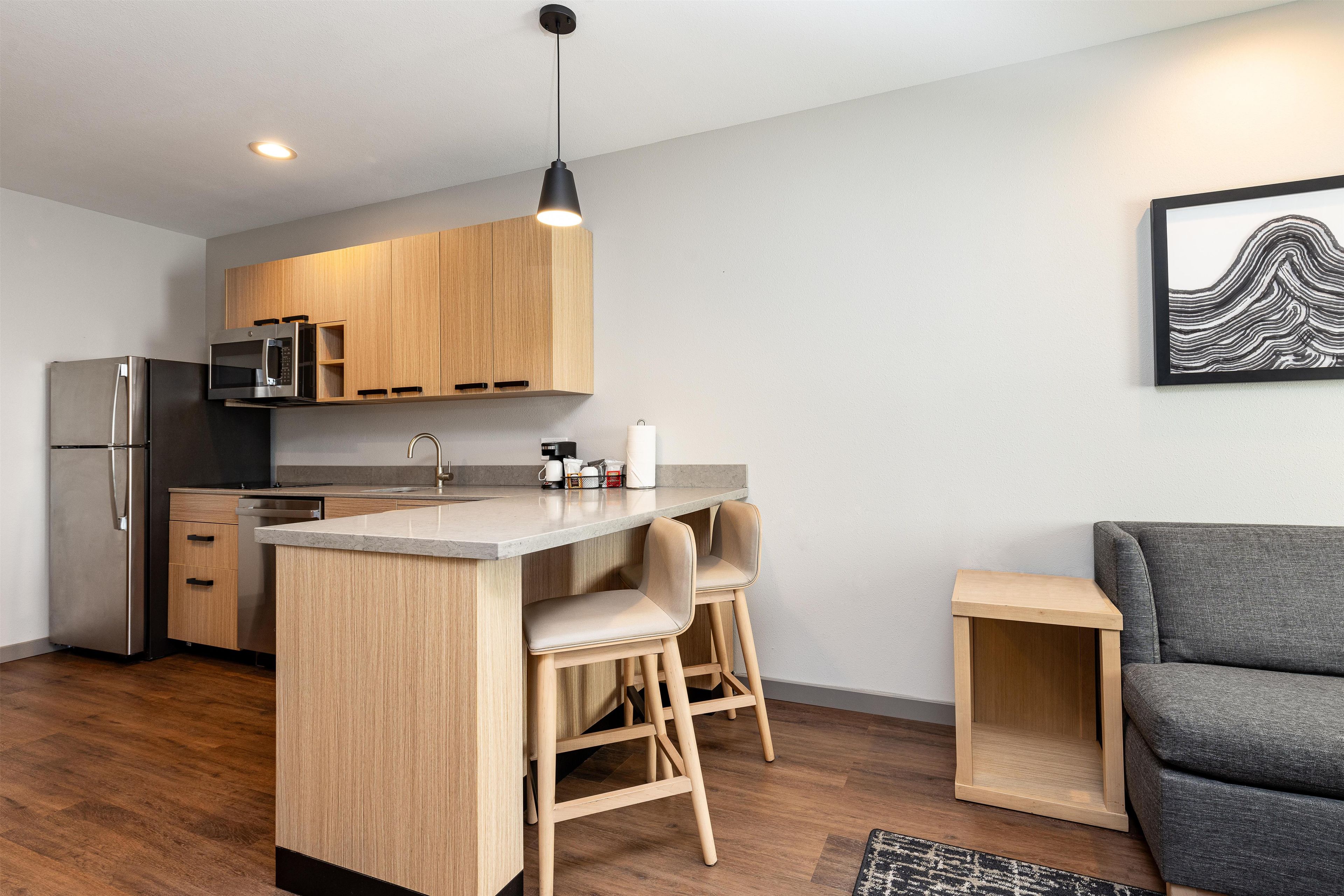 A modern kitchen with wooden cabinets, a built-in microwave, a stainless steel refrigerator, and a bar area with stools.