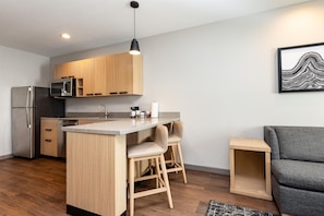 A modern kitchen with wooden cabinets, a built-in microwave, a stainless steel refrigerator, and a bar area with stools. - Hyatt Place Munster (Munster)