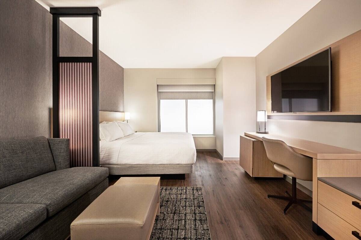 Ett modernt hotellrum med en säng, en soffa, ett skrivbord och en tv.