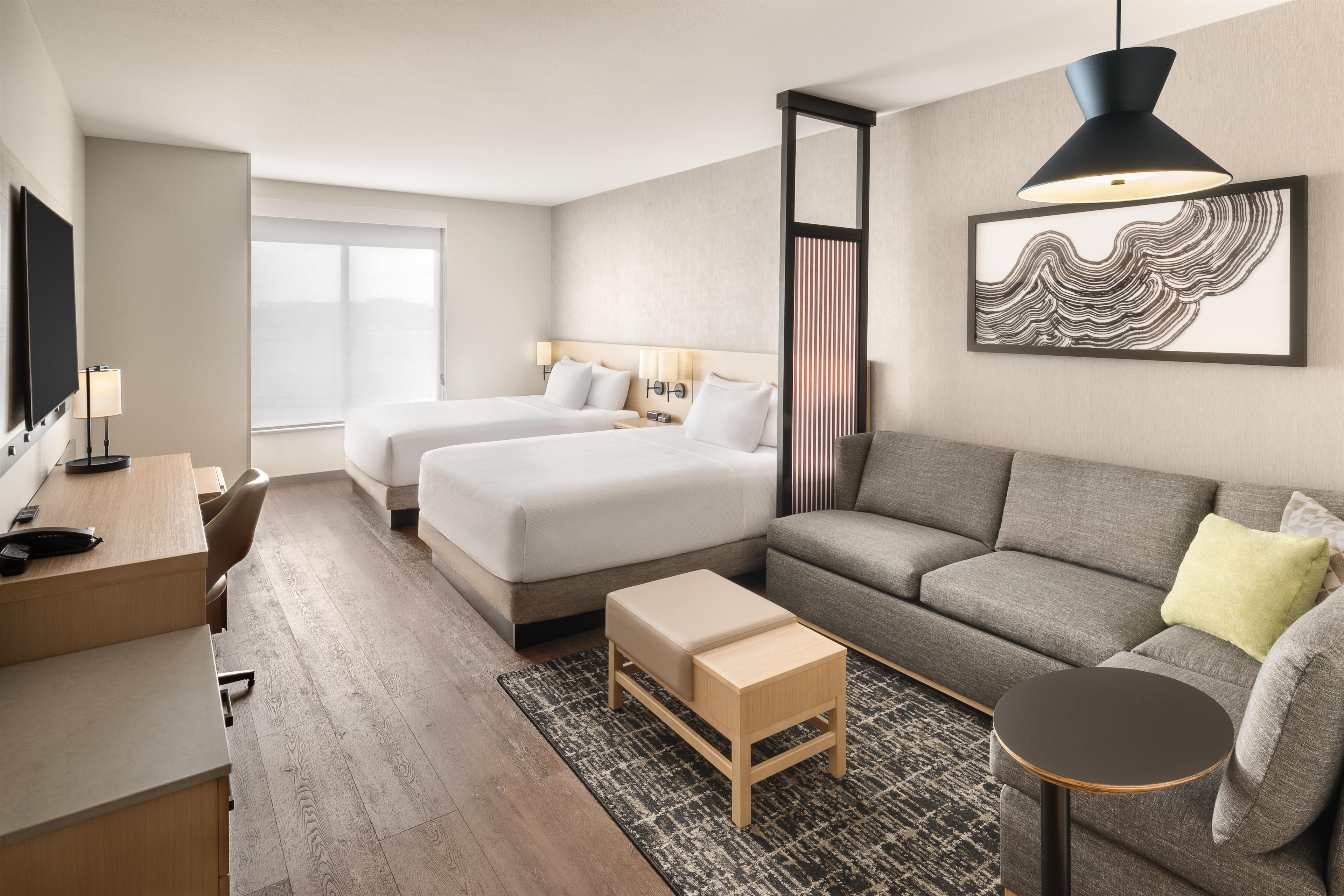 A hotel room with two beds, a sofa, a desk, and a television.