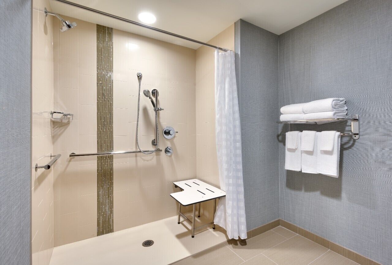 A shower with a glass door, a towel rack with folded towels, and a small table.