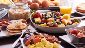 Un bufé de desayuno con panqueques, huevos revueltos, tocino y una variedad de frutas y verduras.