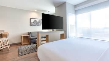 A hotel room with a bed, a desk with a flat-screen TV, a chair, and a large window offering a city view.