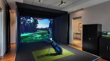 A room with a large screen displaying a golf game, a golf bag, and a cabinet.