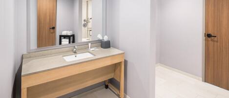 Un baño moderno con un mueble de tocador de madera, un espejo grande y una ducha visible en el reflejo.