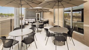 An outdoor patio area with round tables and chairs, large umbrellas, and a view of the street. - Hyatt Place Munster (Munster)