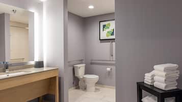 Un baño moderno con tocador de madera, inodoro, una obra de arte enmarco y una pila de toallas.