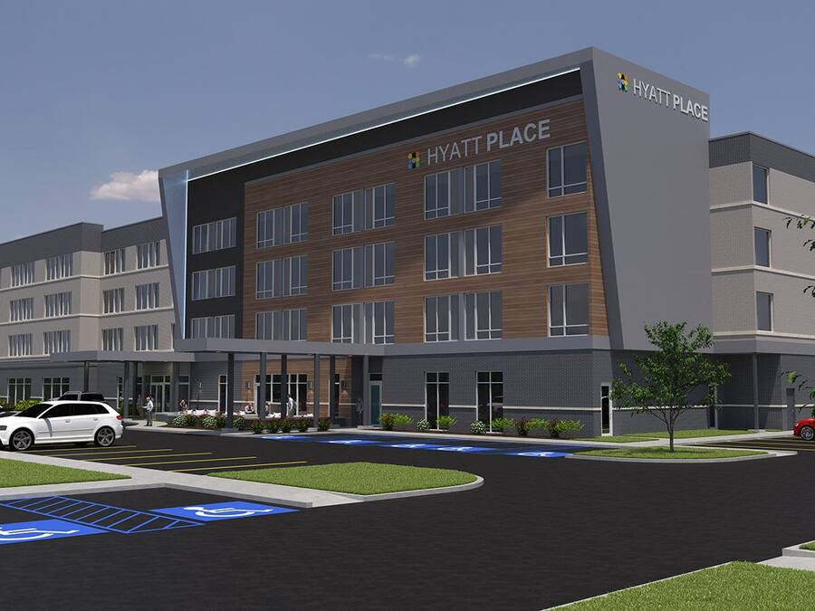 A modern hotel with a multi-story structure, a parking lot with handicapped parking spaces, and a landscaped area with trees.