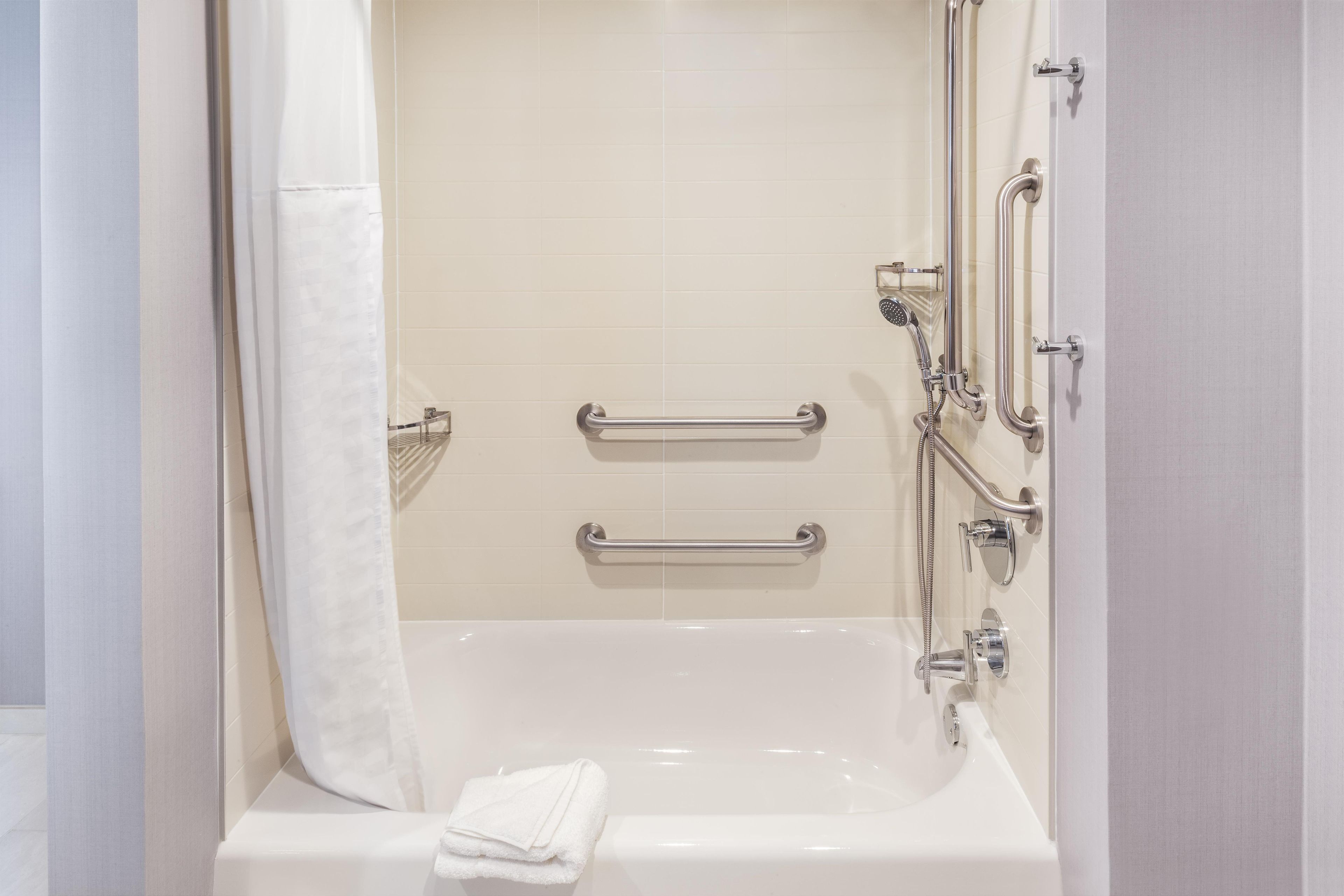 A modern bathroom with a bathtub, grab bars, and a shower head.