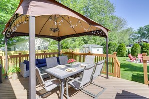 Eine überdachte Terrasse mit Tisch und Stühlen, umgeben von einer Holzterrasse und einem Zaun.