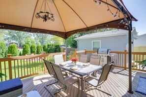 Eine überdachte Terrasse mit Esstisch, umgeben von Stühlen, und einem Grill im Hintergrund.