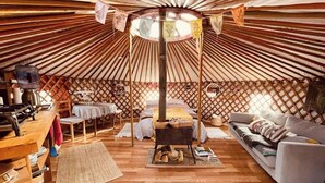 Interior de una yurta con un hogar central, mobiliario de madera y una zona de estar acogedora.