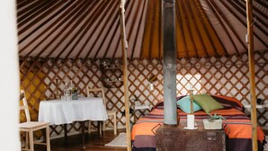 Acogedor interior de una yurta con una cama, una mesa y un estufa de leña.