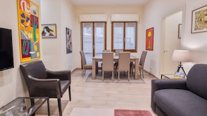 A living room with a sofa, a TV, and a dining area with chairs and a table.