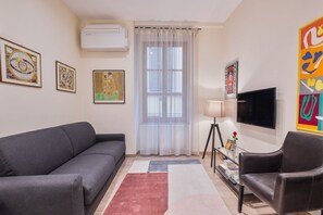 A living room with a grey sofa, a black leather chair, a TV, and artwork on the walls.