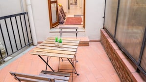 A patio with a wooden table and benches, potted plants, and a view of a hallway.