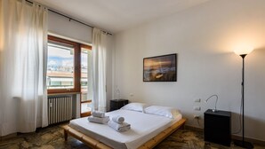 Una camera da letto con un letto, un comodino, una lampada, un quadro e vista dalla finestra.