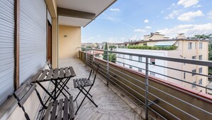 Un balcone con vista su edifici, una persiana chiusa e un tavolo con sedie.