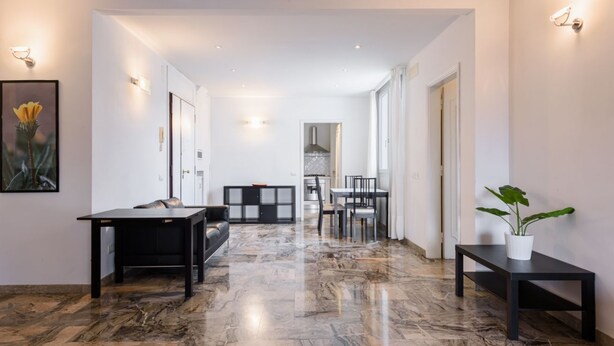 Un interno moderno con pavimento in marmo, una zona pranzo e una cucina visibile attraverso un'apertura.