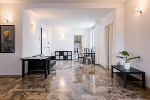A modern interior with a marble floor, a dining area, and a kitchen visible through an open door.