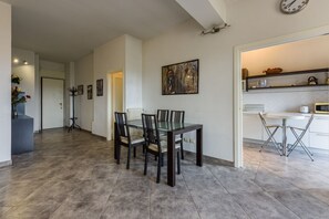 A dining area with a glass table and chairs, a kitchen with white cabinets, and a clock on the wall.