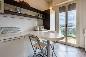 Une cuisine avec un plan de travail blanc, une chaise en métal et une vue à travers une porte vitrée.