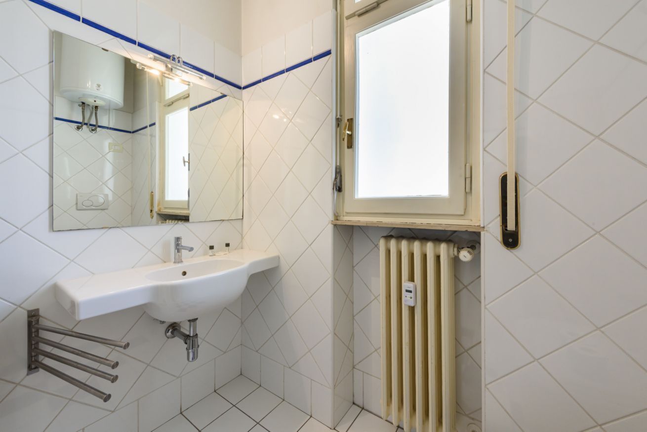 A bathroom with a white sink, a mirror, a window, and a radiator.