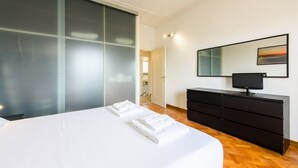 Un dormitorio con una cama, un aparador negro, un televisor y un armario con puerta corredera.