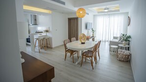 Un salon moderne avec une table à manger ronde, des chaises en osier, un ventilateur de plafond et une grande fenêtre avec des rideaux.