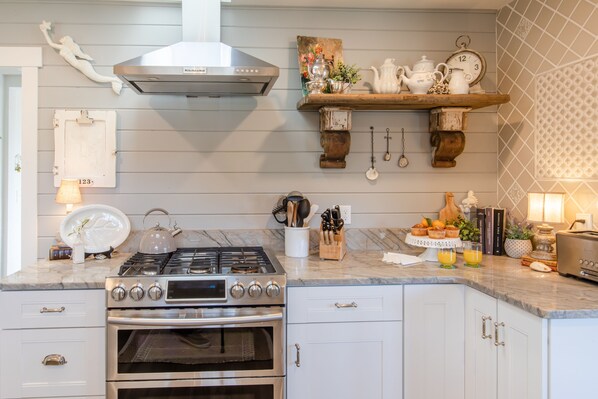 A kitchen with a gas stove, oven, and a wooden shelf with kitchenware.
