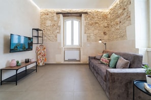 A living room with a stone wall, a sofa, a TV, a bench, and a door leading to a balcony.