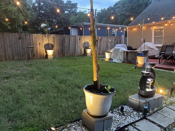 Relax in a serene backyard oasis with a well-manicured lawn, water feature, and comfortable patio seating.