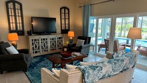 A living room with a sofa, armchairs, a TV, and a pool view. - Stay in The Villages at your pool house with cart! (Wildwood)