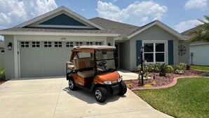 A residential house with a garage, a golf cart parked in the driveway, and a well-maintained lawn. - Stay in The Villages at your pool house with cart! (Wildwood)