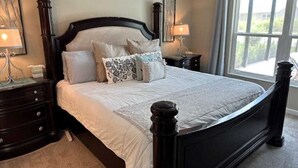 A bedroom with a large bed, dark wooden headboard, two bedside tables with lamps, and a window with curtains. - Stay in The Villages at your pool house with cart! (Wildwood)