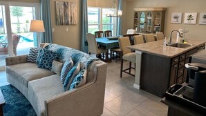 A modern kitchen with a central island, a dining area with a table and chairs, and a living room with a sofa and a lamp. - Stay in The Villages at your pool house with cart! (Wildwood)