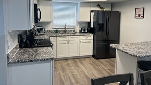 A kitchen with white cabinets, a black refrigerator, a microwave, and a granite countertop. - Lovely Apartment Close to the Beach ! (Cape Canaveral)